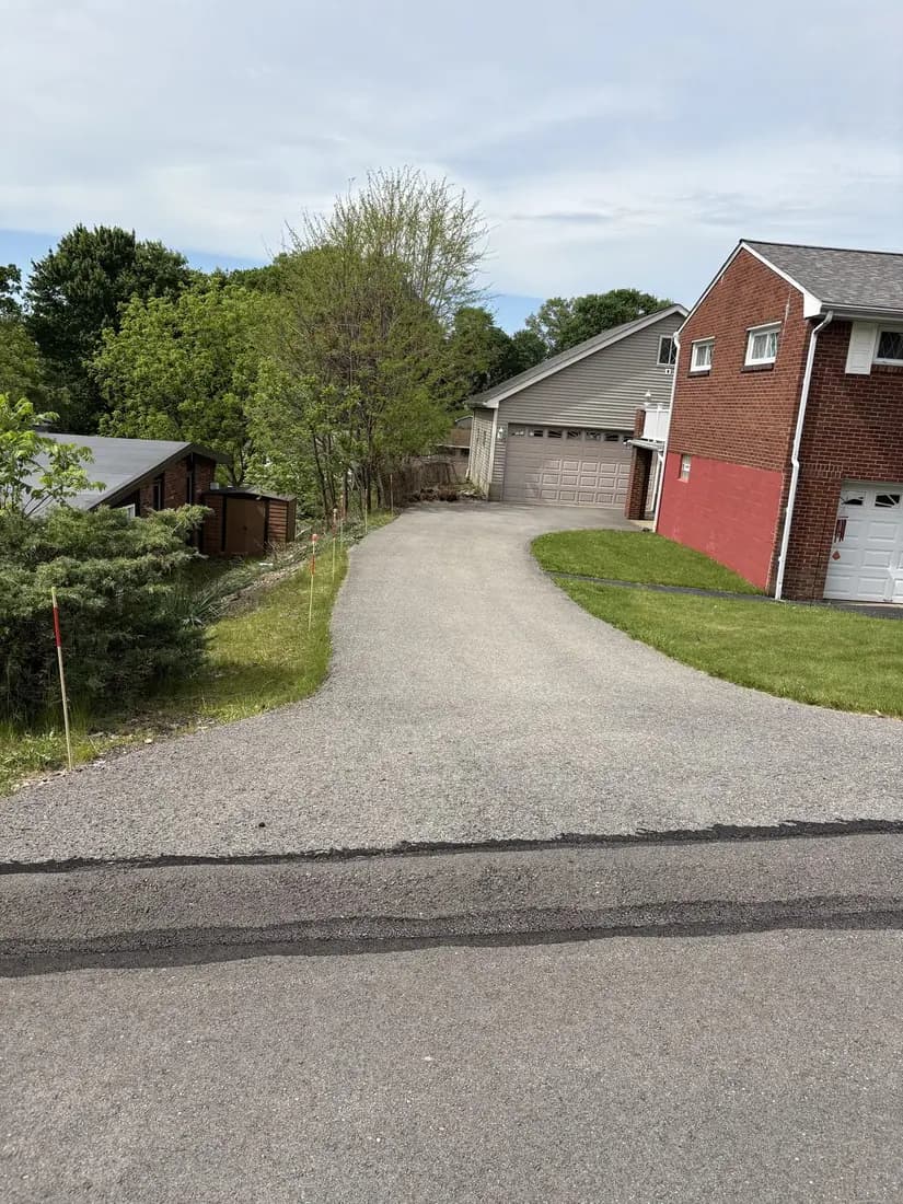 Faded gray asphalt driveway before sealcoating at a red-brick home