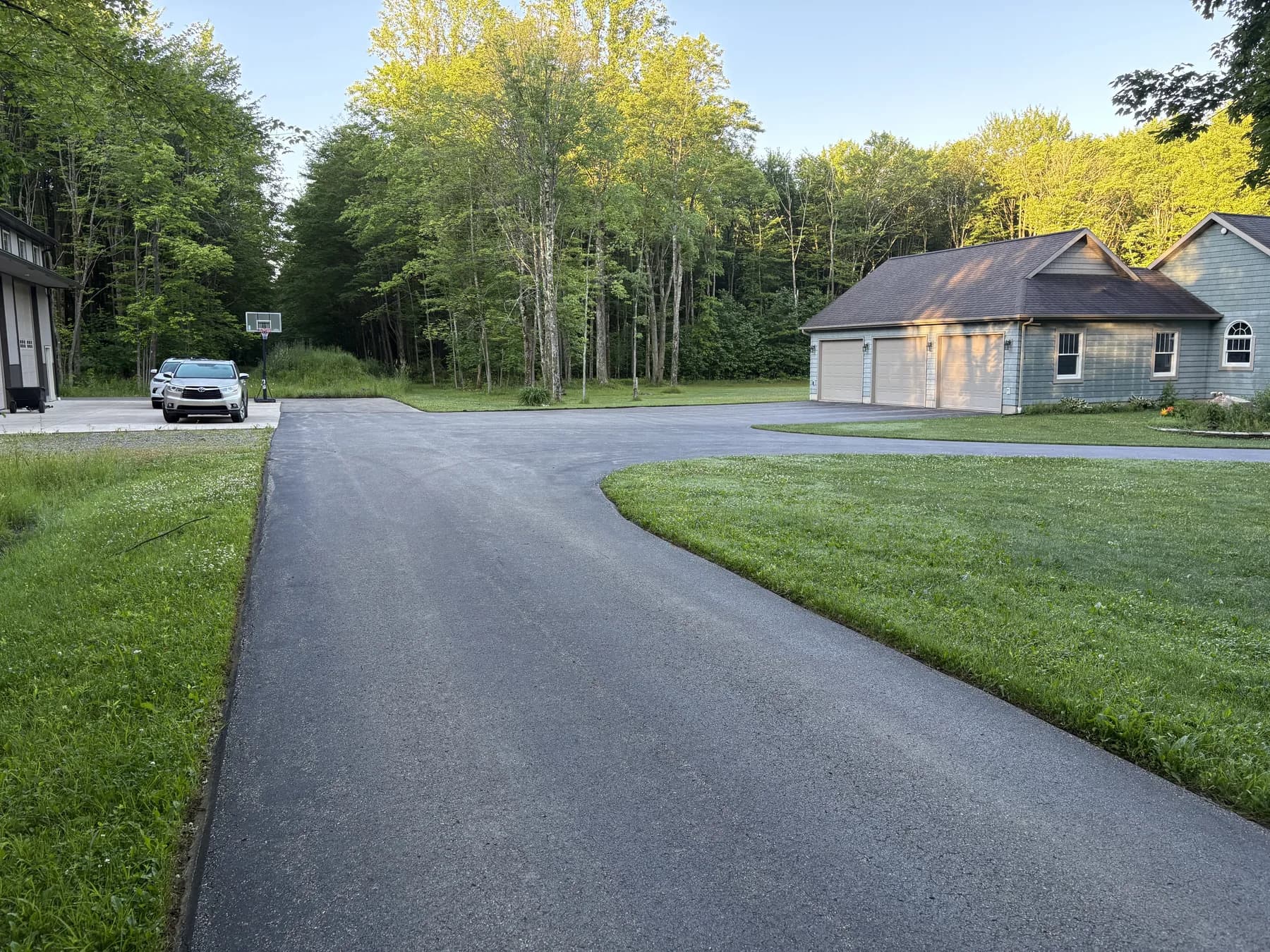 Faded gray asphalt driveway before sealcoating at a wooded blue home