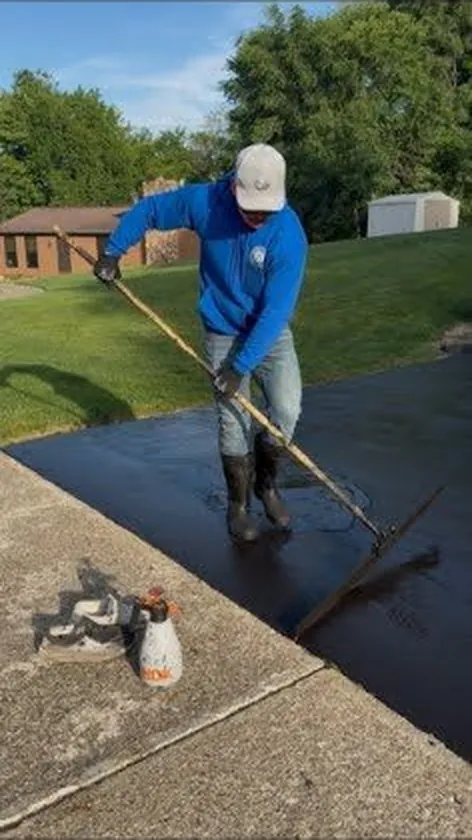Tommy hand-applying asphalt sealer with a squeegee