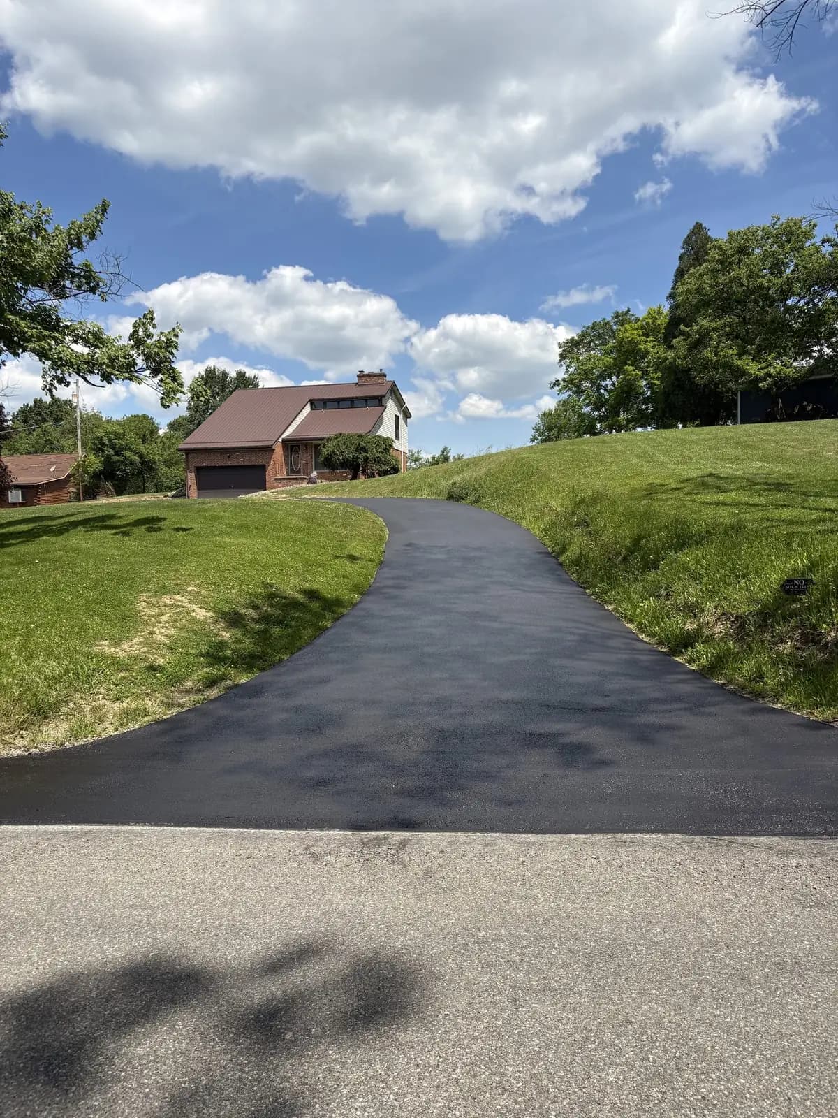 Freshly sealcoated asphalt driveway curving through a green lawn